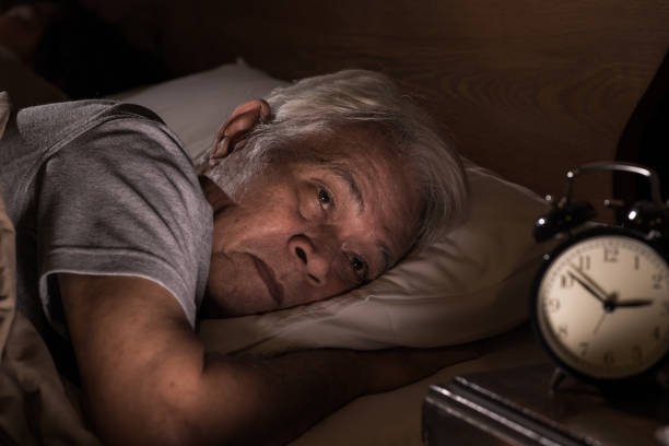 Homem acima dos 60 anos com insônia olhando para o relógio durante a noite — distúrbios do sono comuns após os 40